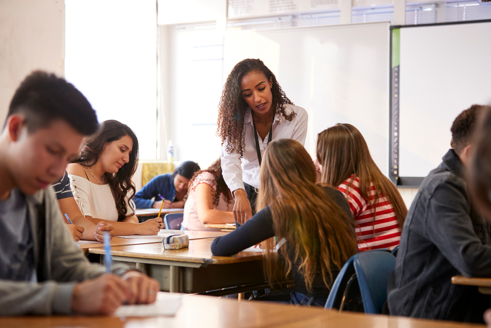 Female High School Teacher Standing by Student Table Teaching 